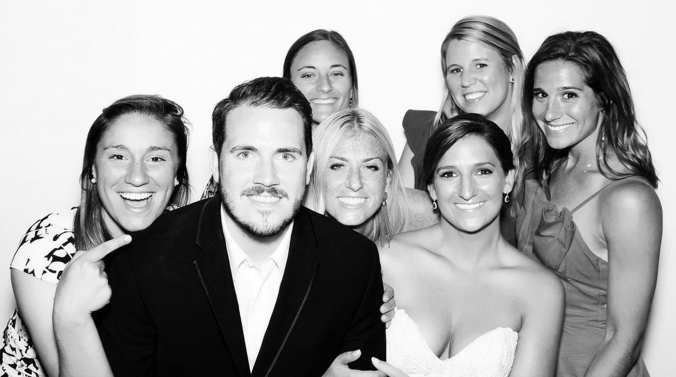 Seven wedding guests smiling together in a black-and-white photo booth portrait
